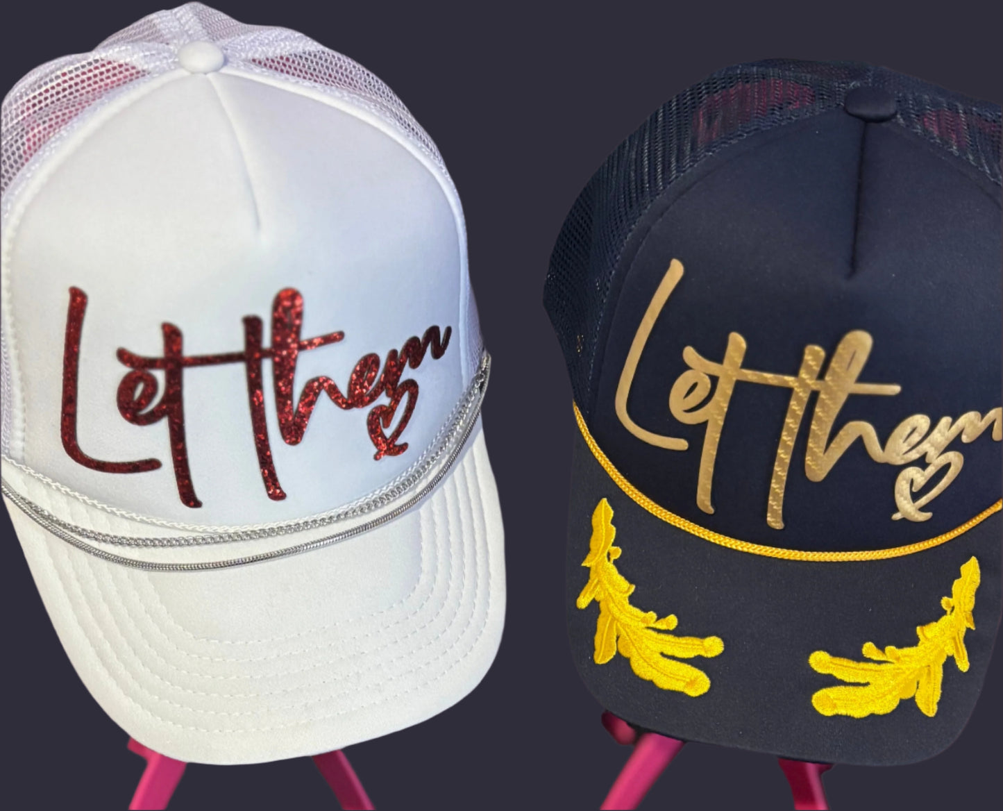 Two hats with 'Let them' text on stands against a blurred background