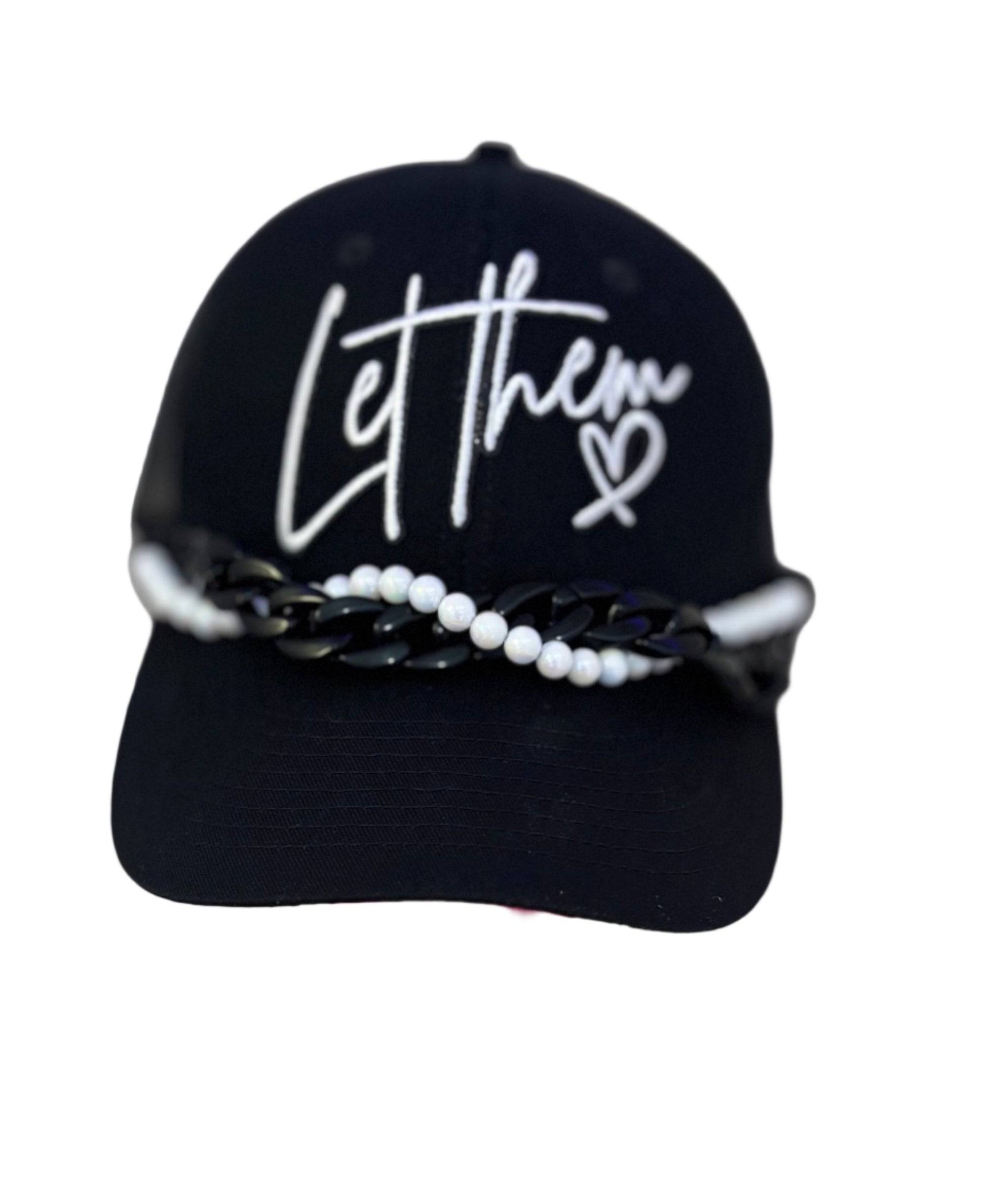 Black cap with 'Let them' text on a stand against a white background